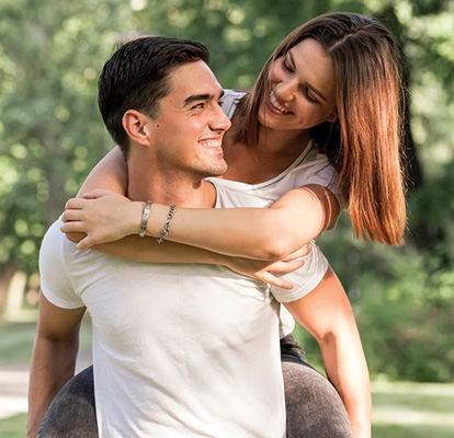 Una pareja feliz pasea en bicicleta por un campo iluminado por el sol; la mujer sonríe y levanta el brazo mientras el hombre conduce.